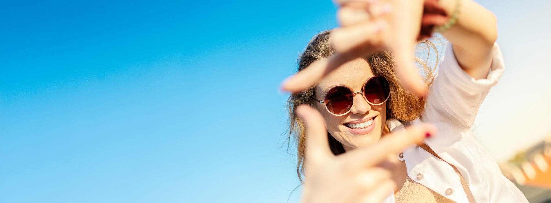 A woman taking a selfie with her hand raised against a blue sky background.