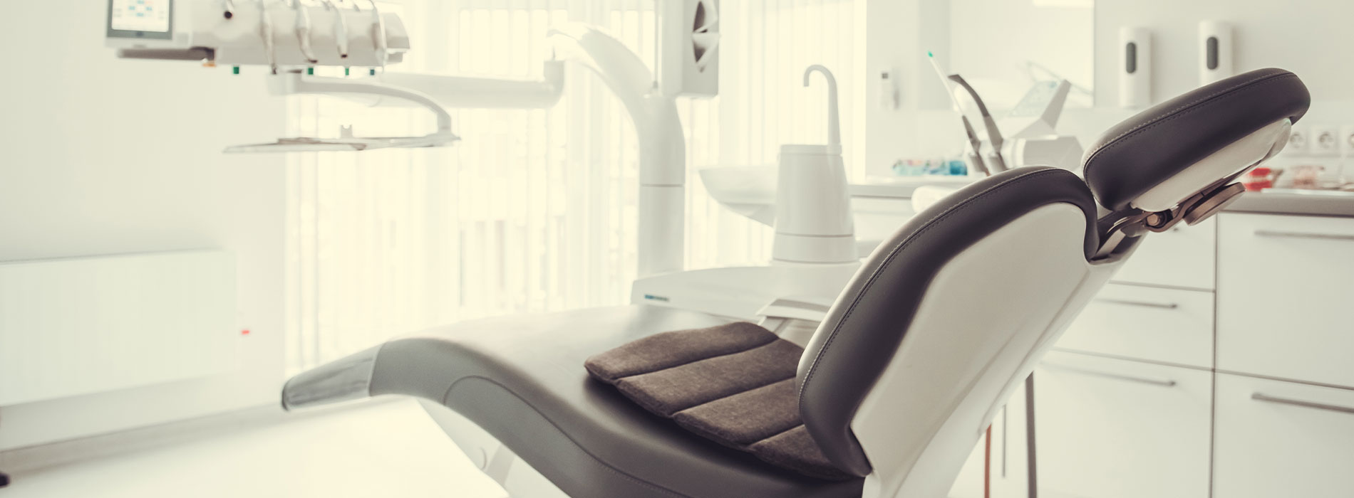 The image shows a modern dental chair with a sleek design, situated in a well-lit dental office setting.
