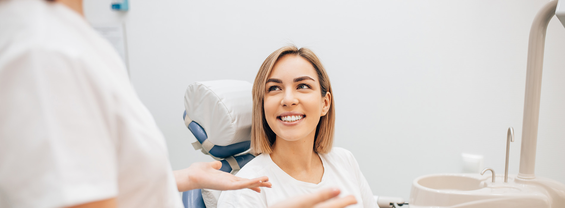 The image shows a woman sitting in a dental chair with her eyes closed, smiling slightly, while receiving dental care from a professional who appears to be a dentist.