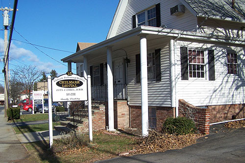 The image shows a two-story building with a sign on the front, likely indicating its function, set against an overcast sky.