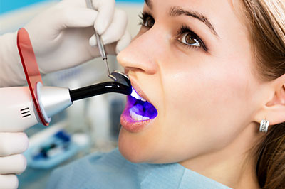 The image shows a person receiving dental care with an electric toothbrush  they are seated in a dental chair, wearing a protective gown and visor, while a dental professional performs the procedure.