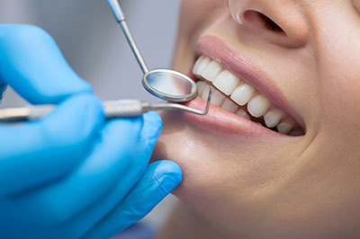 An individual receiving dental care with a smile, while a dental professional works on their teeth using specialized tools.