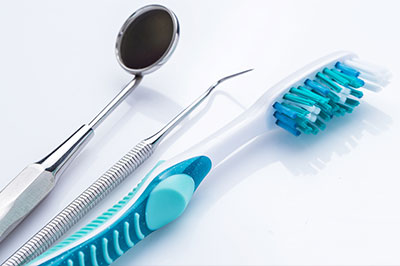 The image shows dental tools including a toothbrush with blue bristles and a pair of scissors on a white surface, suggesting a dental care setting.