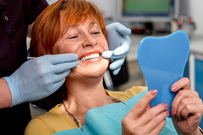 A woman with red hair sits in a dental chair, smiling at the camera, while a dentist holds up an impression mold to her teeth.