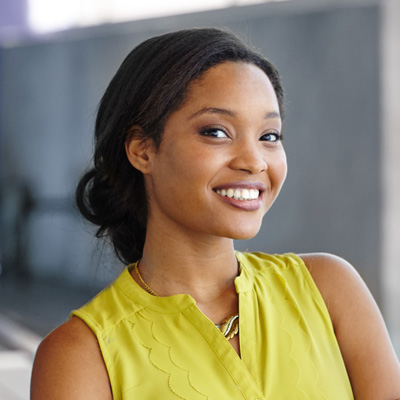 A woman with dark hair, wearing a yellow top and smiling broadly at the camera.
