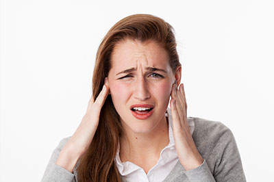 The image shows a person with their hand on their ear, appearing to be in pain or discomfort, with a surprised expression.