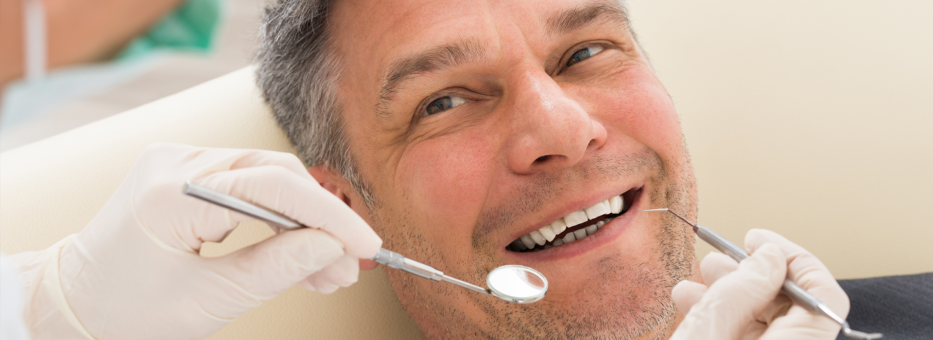 A man sitting in a dental chair with a smile, receiving dental care while wearing a surgical mask.