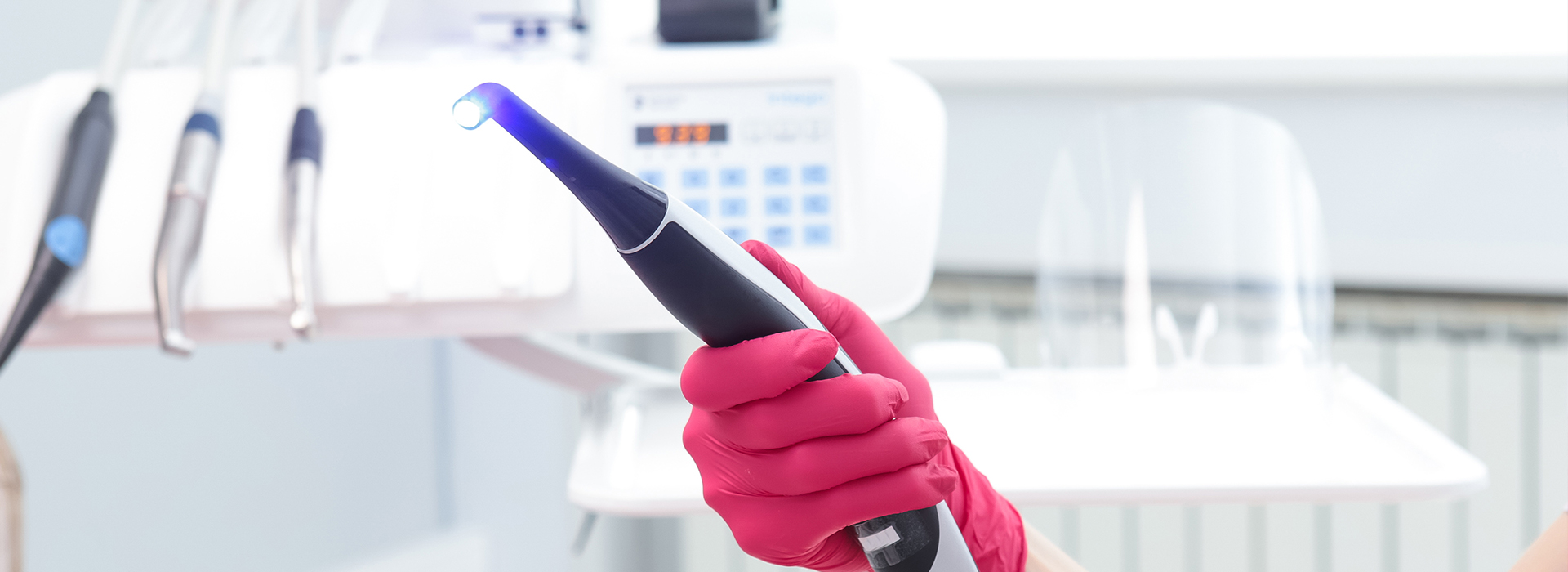 The image shows a person wearing red gloves holding an electronic device with a blue light against the backdrop of a laboratory setting.