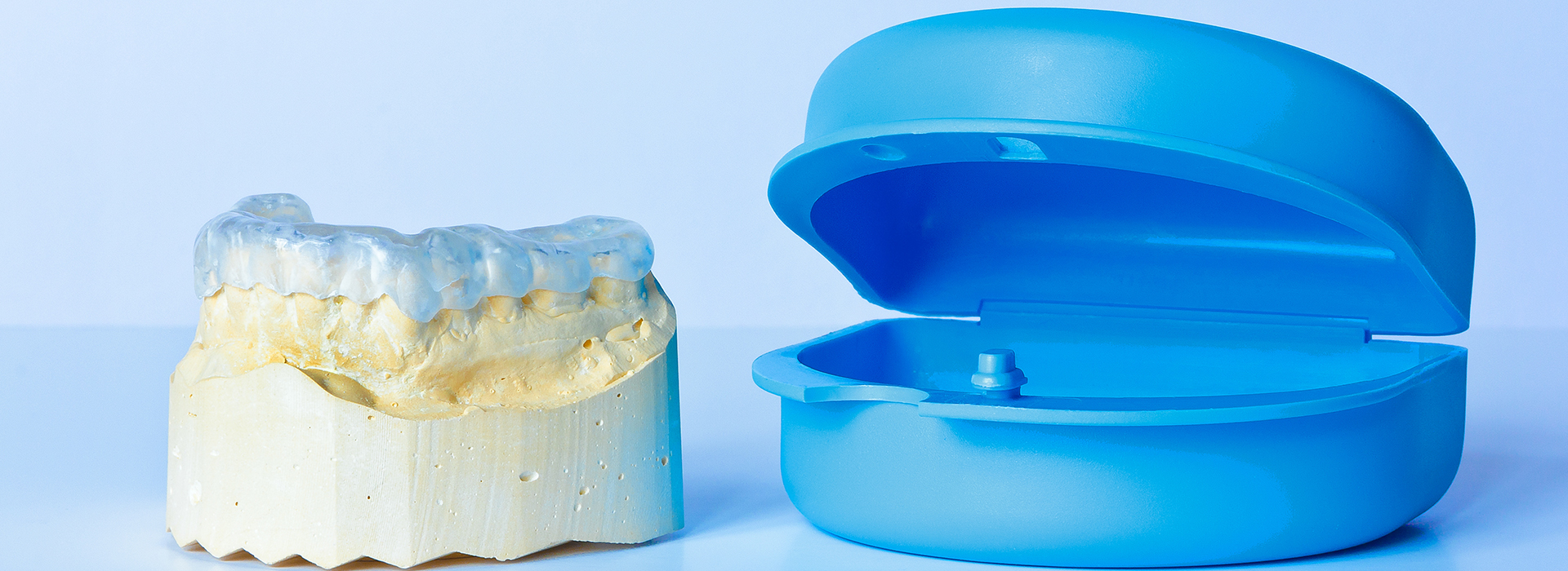The image shows a blue dental implant next to a white dental crown, both resting on a plain background.