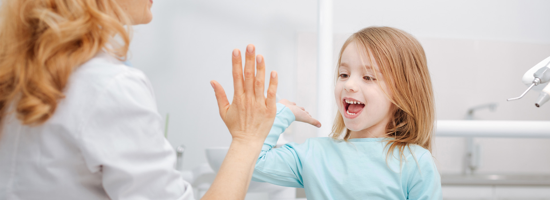A young girl with blonde hair is waving at someone while standing next to an adult woman who is smiling and clapping her hands.