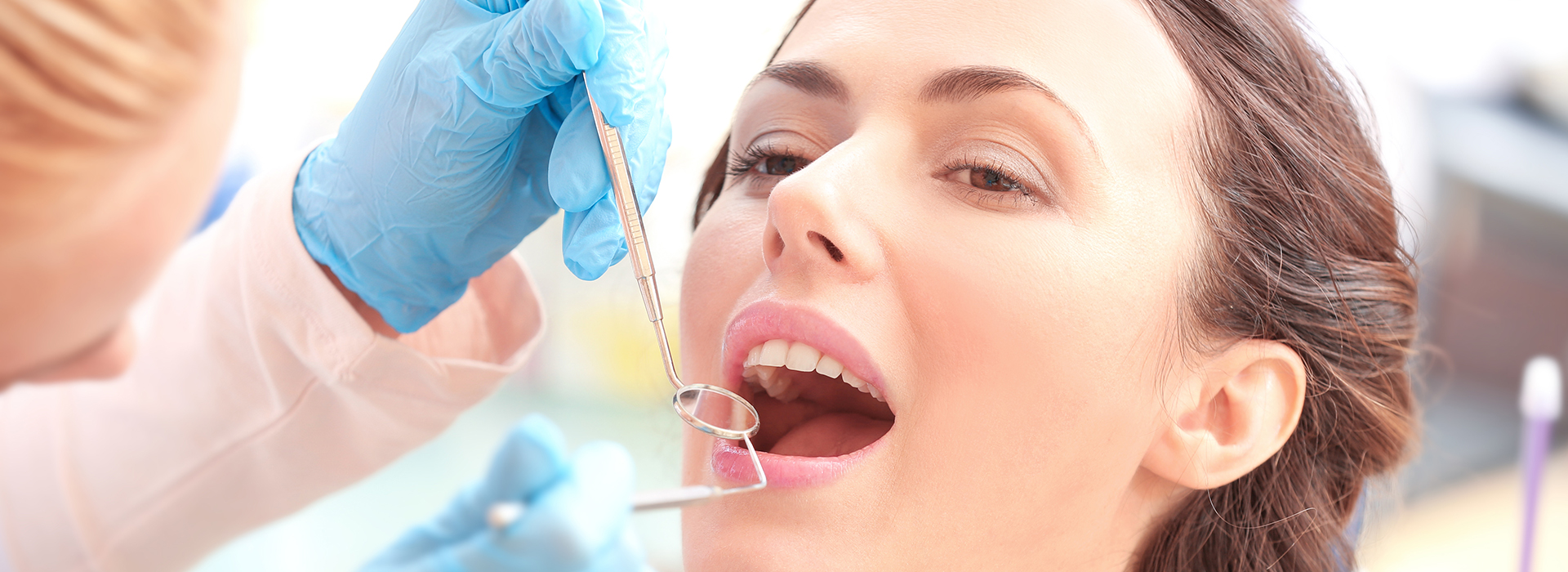 The image shows a woman receiving dental treatment with visible dental tools being used by a dental professional.