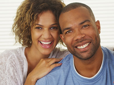The image shows a man and woman posing together with smiles  they appear to be a couple celebrating a moment, likely a wedding given the attire and setting.