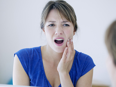 Woman with hand on her face expressing concern or worry while looking at her reflection in the mirror.