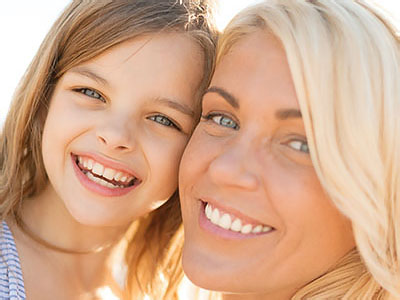 The image shows a woman and a young girl smiling at the camera, with the woman appearing to be a mother and the girl her daughter.