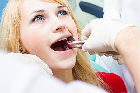 A young woman receiving dental care with a dentist performing a procedure on her teeth while she holds her mouth open.