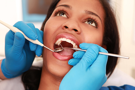 The image shows a person receiving dental care with a pair of hands holding dental instruments near their mouth, which appears to be open during the procedure.