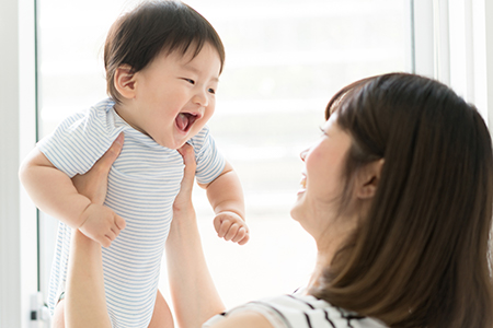 The image shows a woman holding a smiling baby with both hands, looking down at the child with a smile on her face.