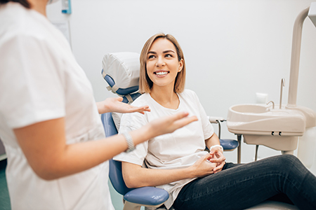 A woman seated on dental chair with a smile, receiving dental care from two professionals who are standing behind her.