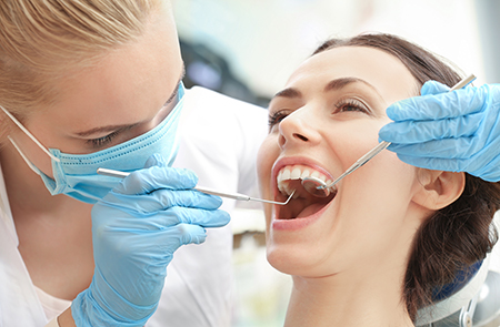 A dental hygienist wearing gloves is performing oral care on a seated patient s teeth.