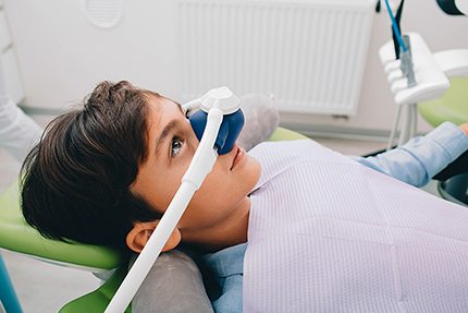 The image shows a young person sitting in a dental chair with a dental device on their face, appearing to be undergoing a dental examination or procedure.