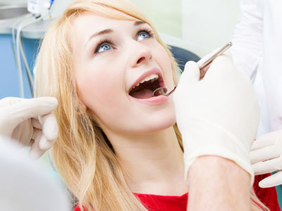 Woman undergoing dental procedure with dentist s hand holding tweezers near her mouth.