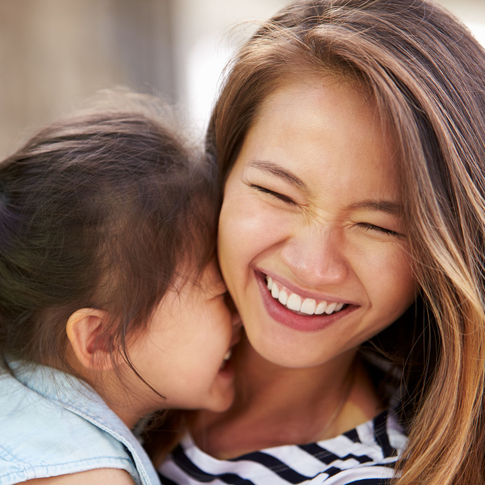 A woman with a wide smile is hugging a child who is also smiling broadly.